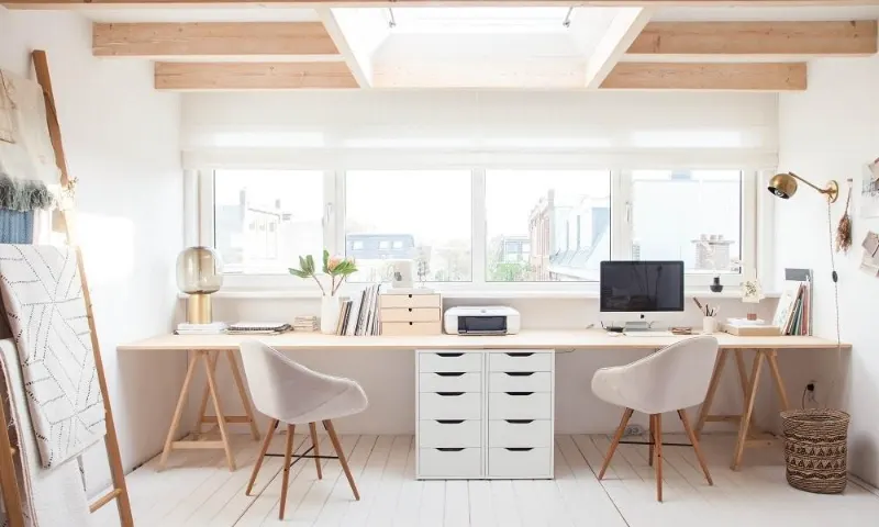 Two office desks near a window with soft daylight and white curtains.
