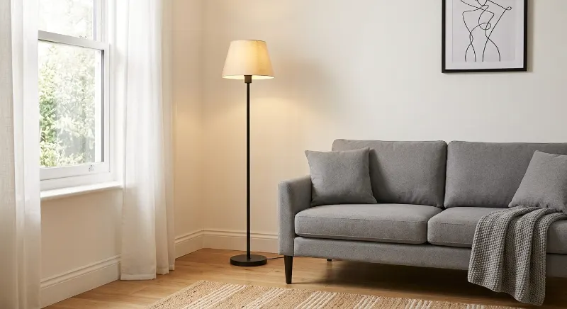 Black floor lamp brightening an empty corner beside a gray sofa.